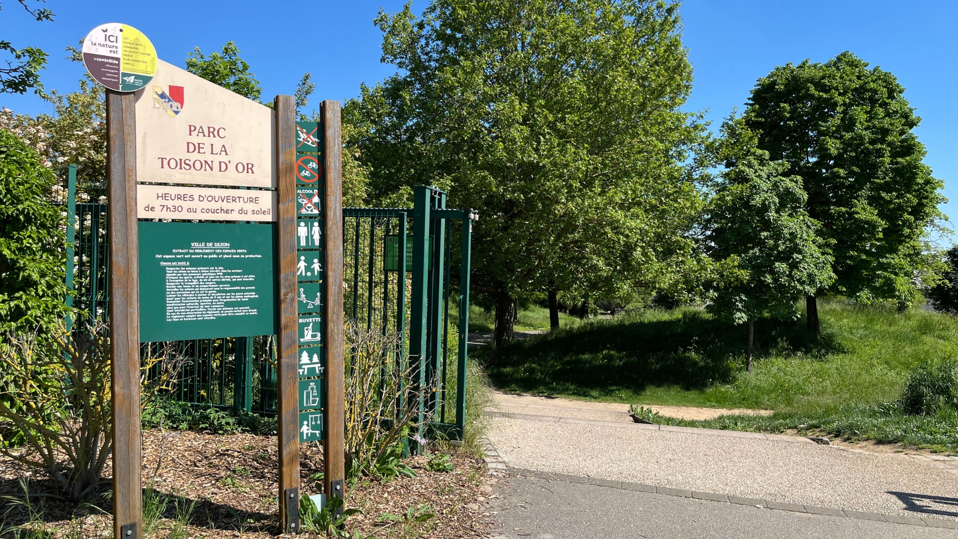 Entrée du Parc de la Toison d’Or avec le panneau d’entrée, des arbres et de l’herbe ensoleillée